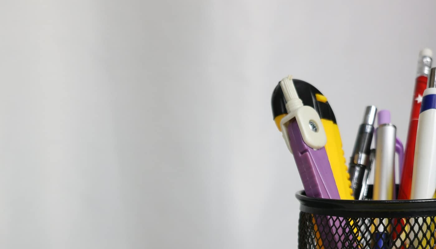 A desk with a calculator, pens in a pen pot and a yellow envelope