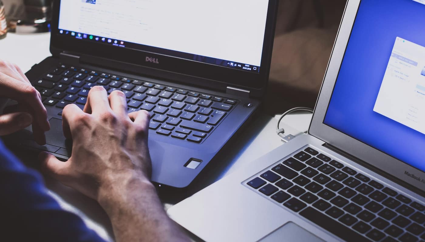 Hands typing on a laptop at a desk with a second laptop beside it
