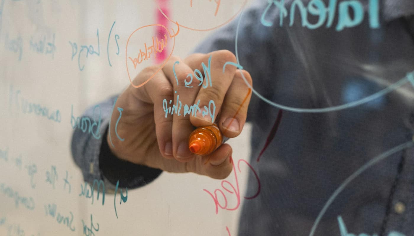 A hand drawing a diagram on a glass whiteboard with a marker