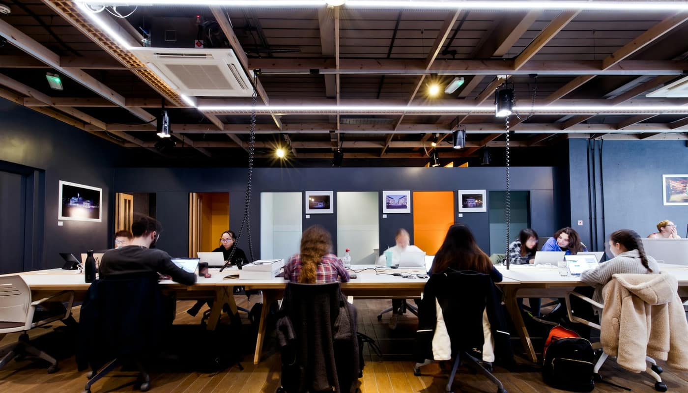 People working side by side at long tables in a dark industrial-style coworking space