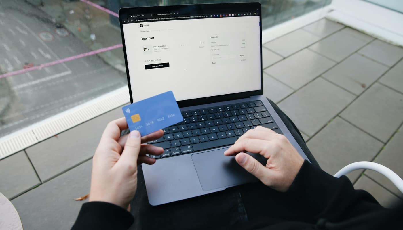 Hands holding a bank card over a laptop keyboard to pay online