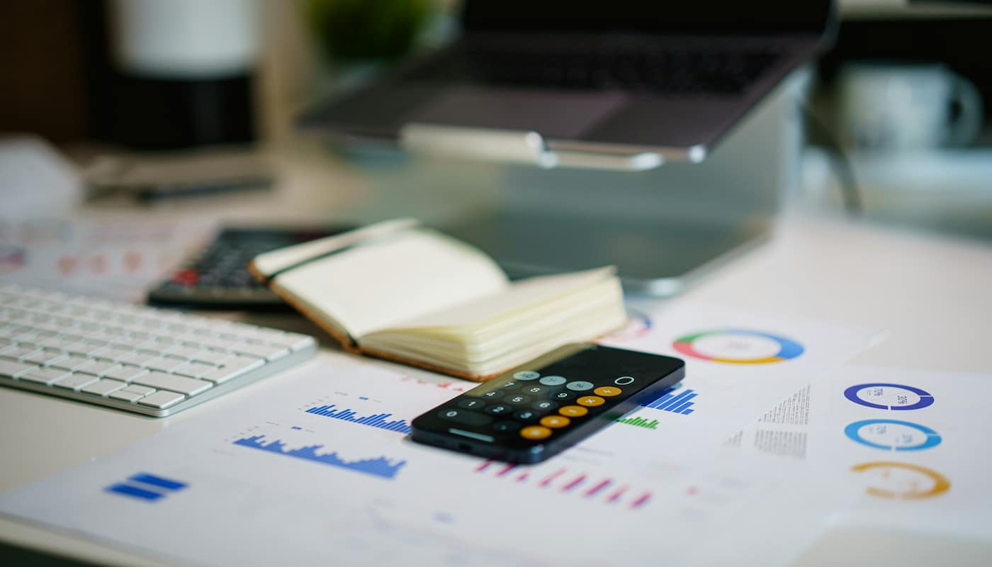 A desk with a calculator, notebook, keyboard and printed charts
