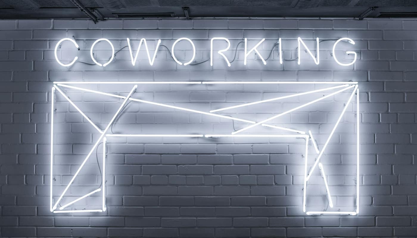 A white neon sign reading Coworking on a dark brick wall