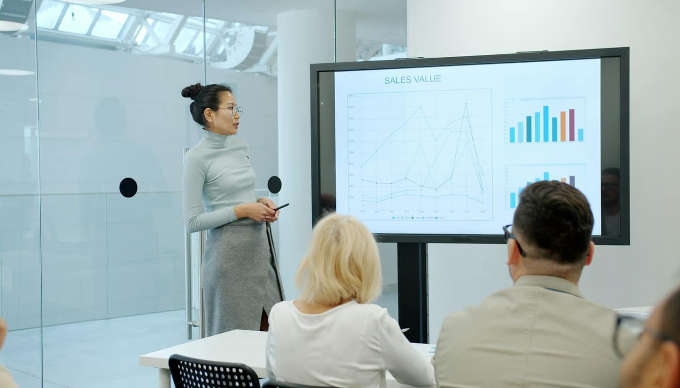 A woman presenting charts on a large screen to colleagues in a bright meeting room