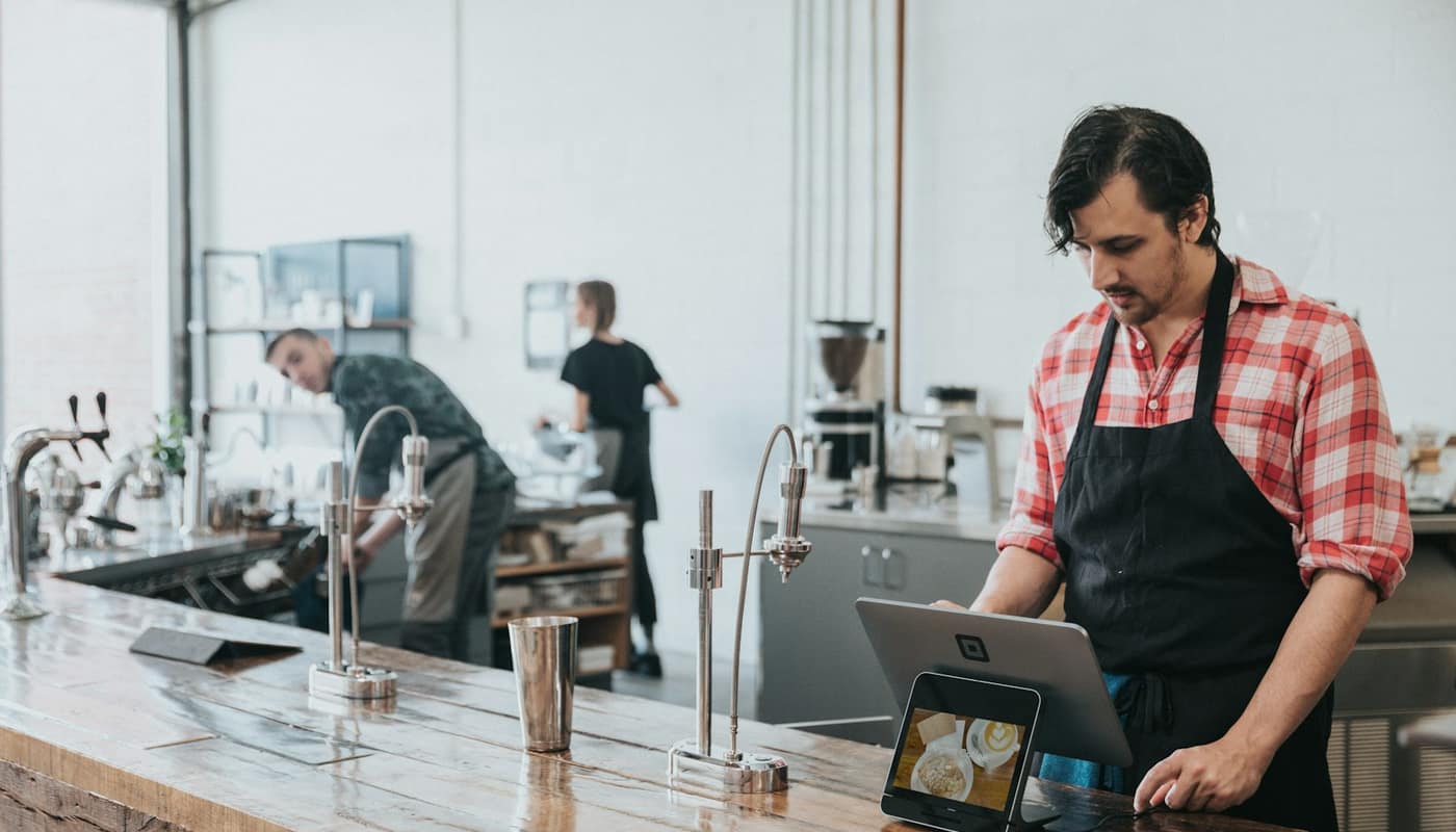 A barista working at a tablet behind a coffee shop counter