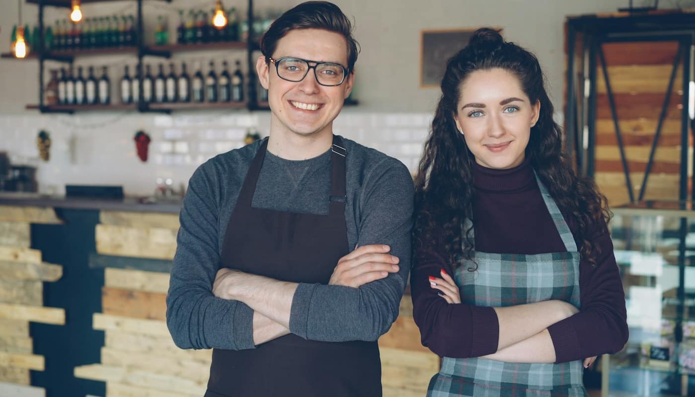 Two cafe owners in aprons standing together with arms crossed, smiling